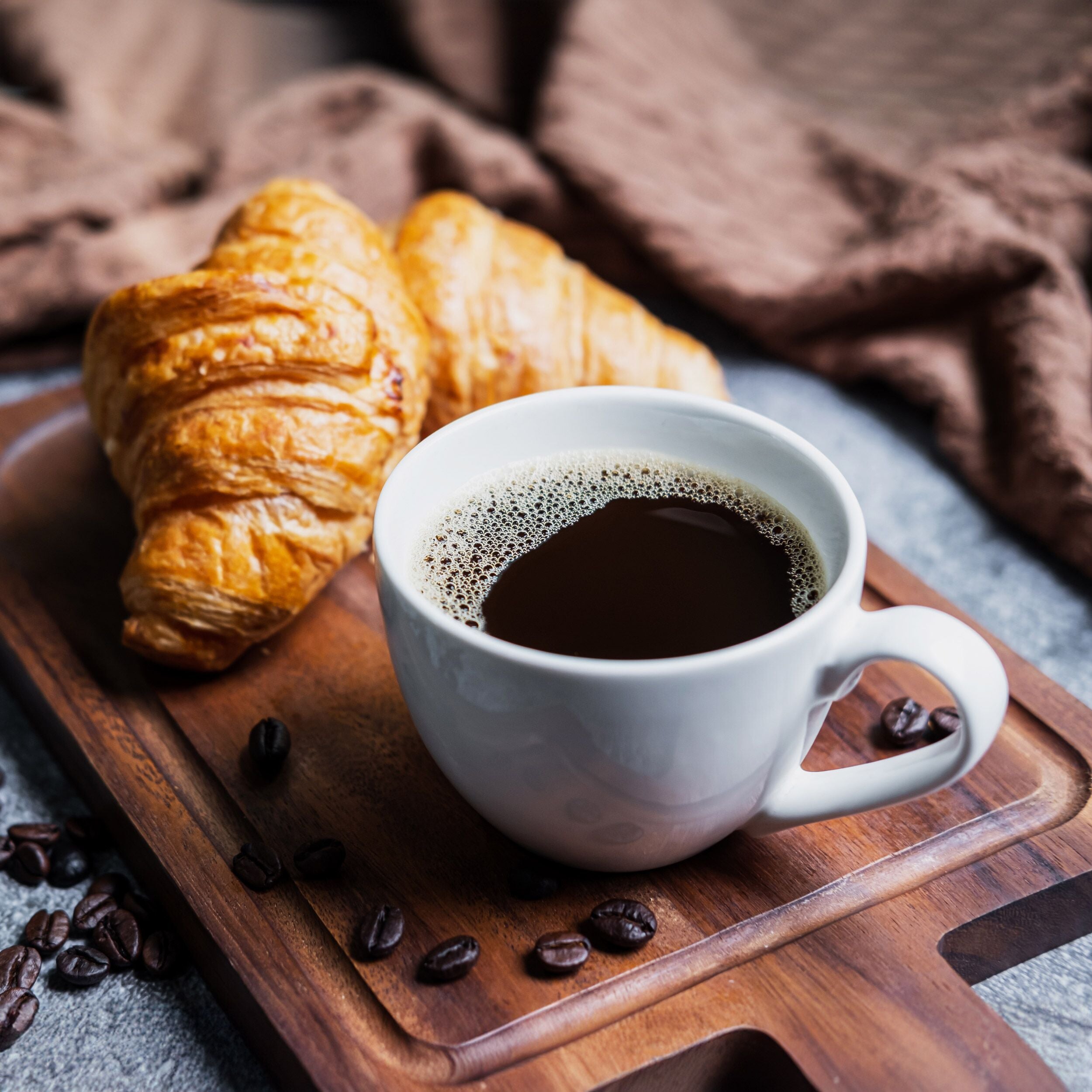 Breakfast with fresh croissants and cup of black coffee on wooden board