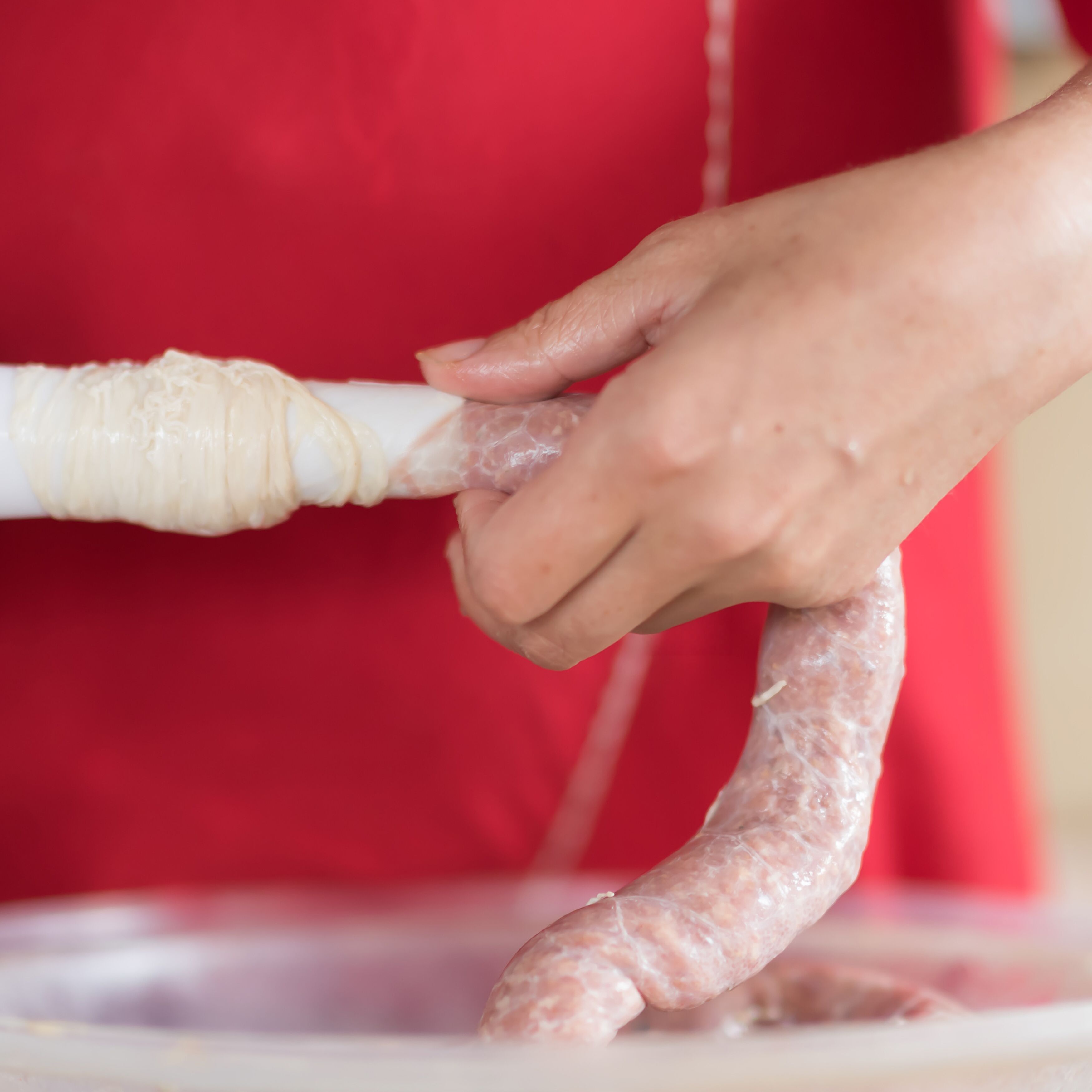 Meat grinder with fresh forcemeat and woman making sausages in kitchen