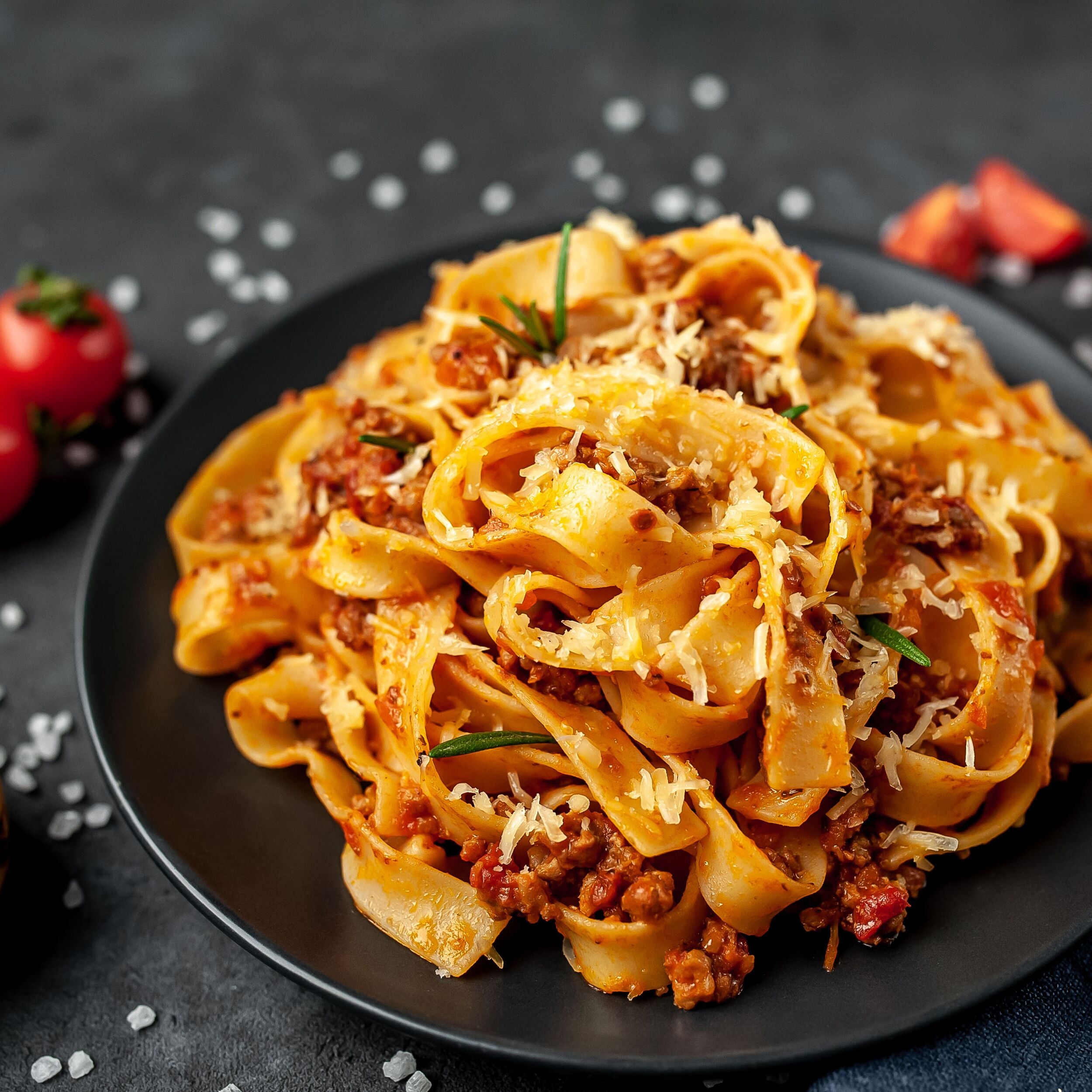 Pasta Bolognese with spices, Italian pasta dish with minced meat and tomatoes in a dark plate on a stone background