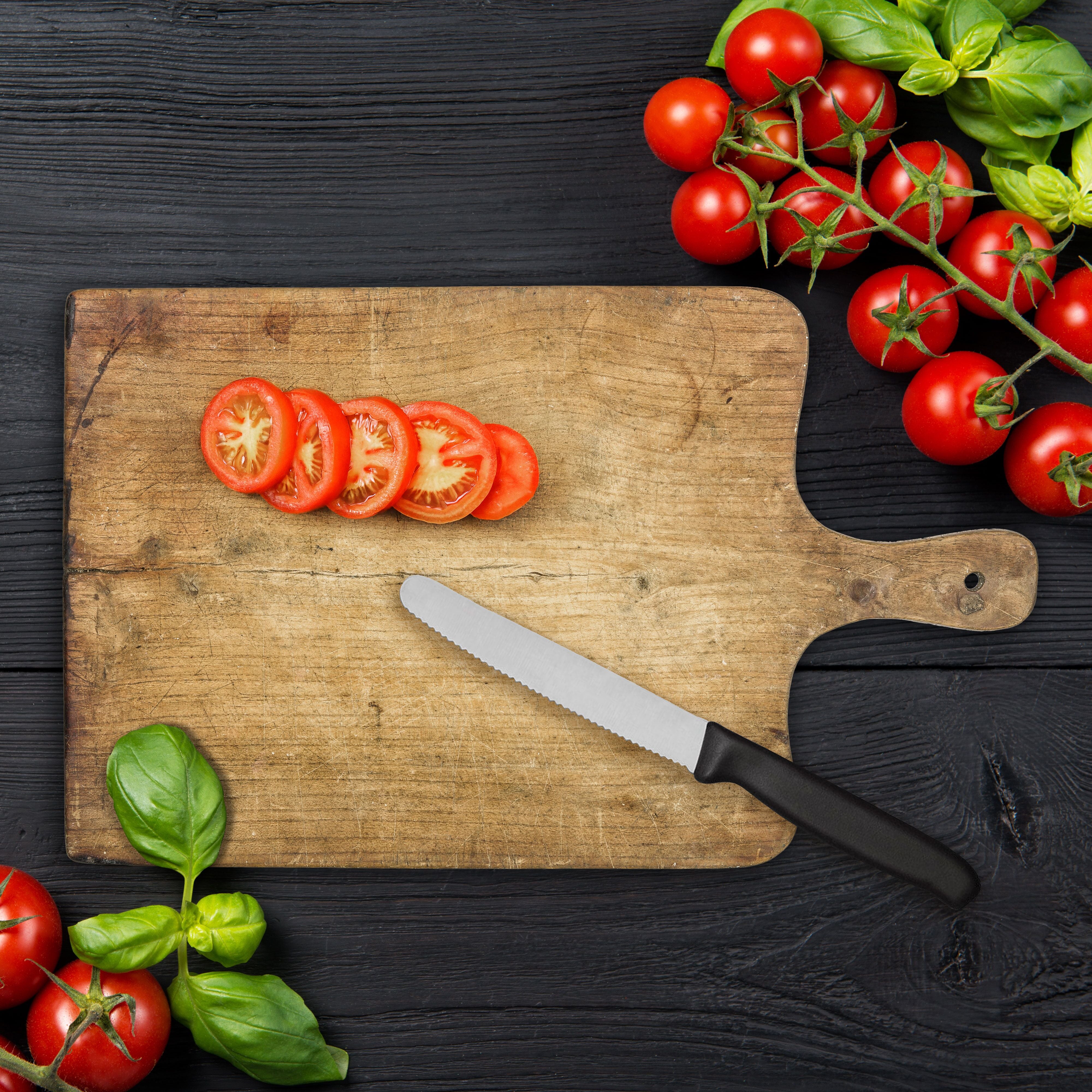 Ripe red cherry tomatoes with fresh basil leaves on black wooden table, top view with copy space